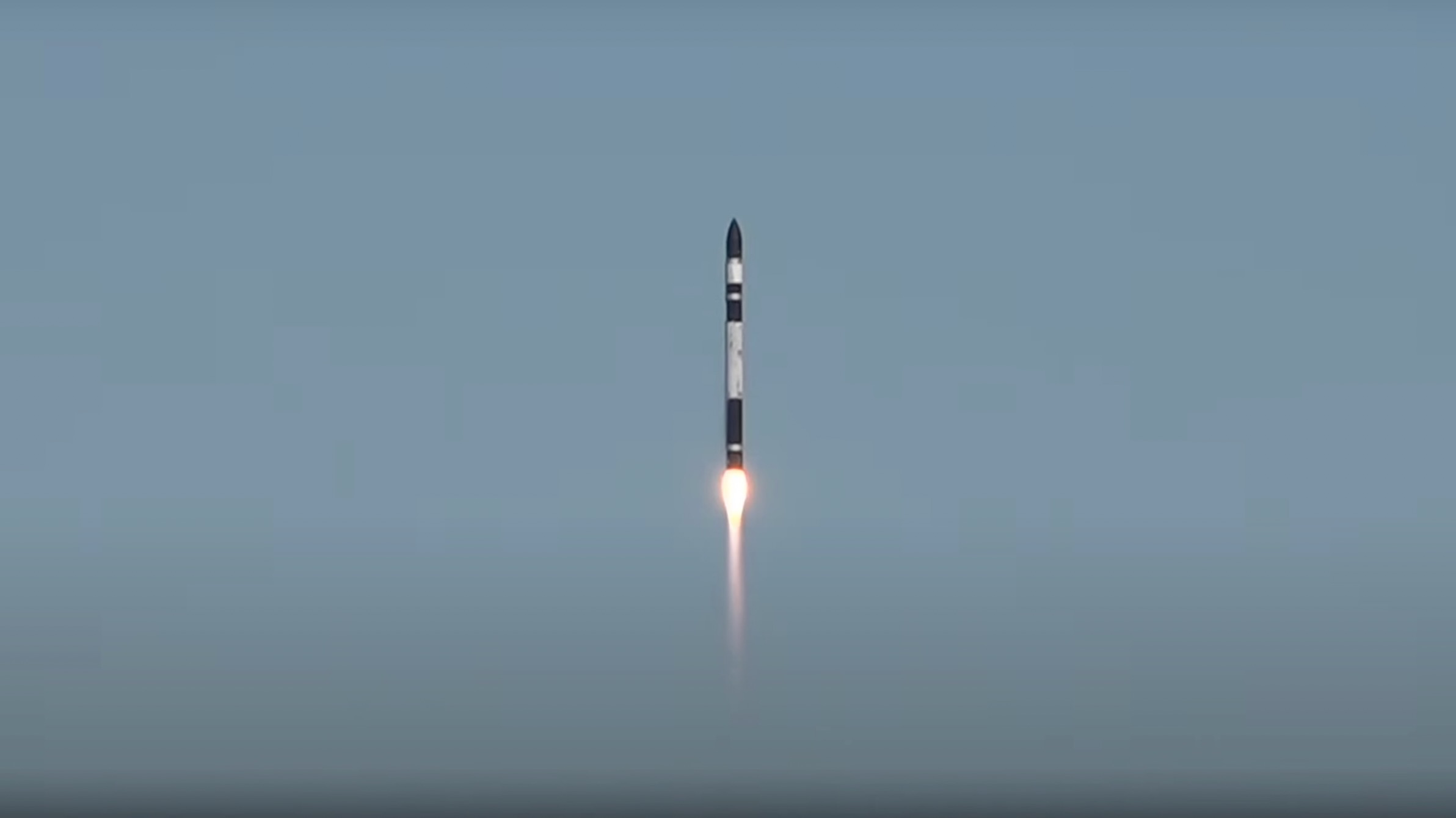 a black and white rocket rises into a clear blue sky