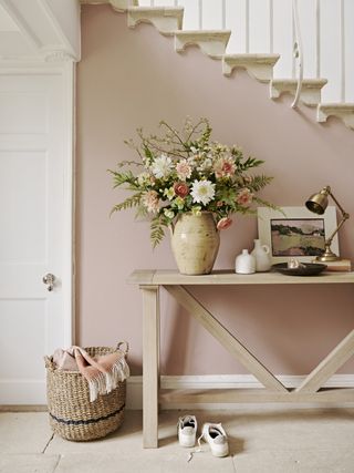 spring style entryway with wood console table, vase of flowers, artwork, brass lamp, stone floor, basket with blanket, white woodwork