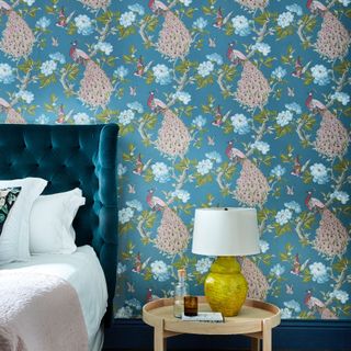 Blue pink and green large motif wallpaper with upholstered headboard and accent side lamp in yellow.