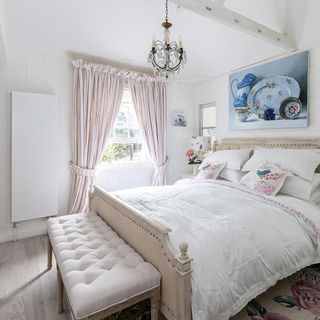 French-style bed with white linen and floral cushions on floral rug next to window with striped curtains