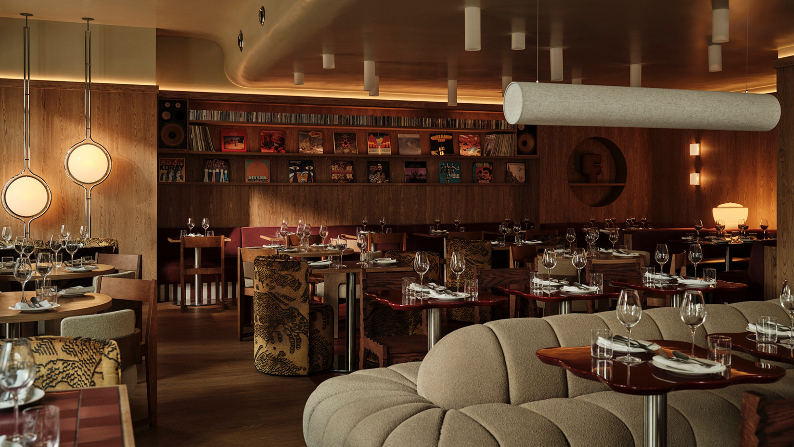 A restaurant with records-filled wooden walls, with spherical sconces, paper lanterns, wood and chrome tables, and eccentric plush fabrics.