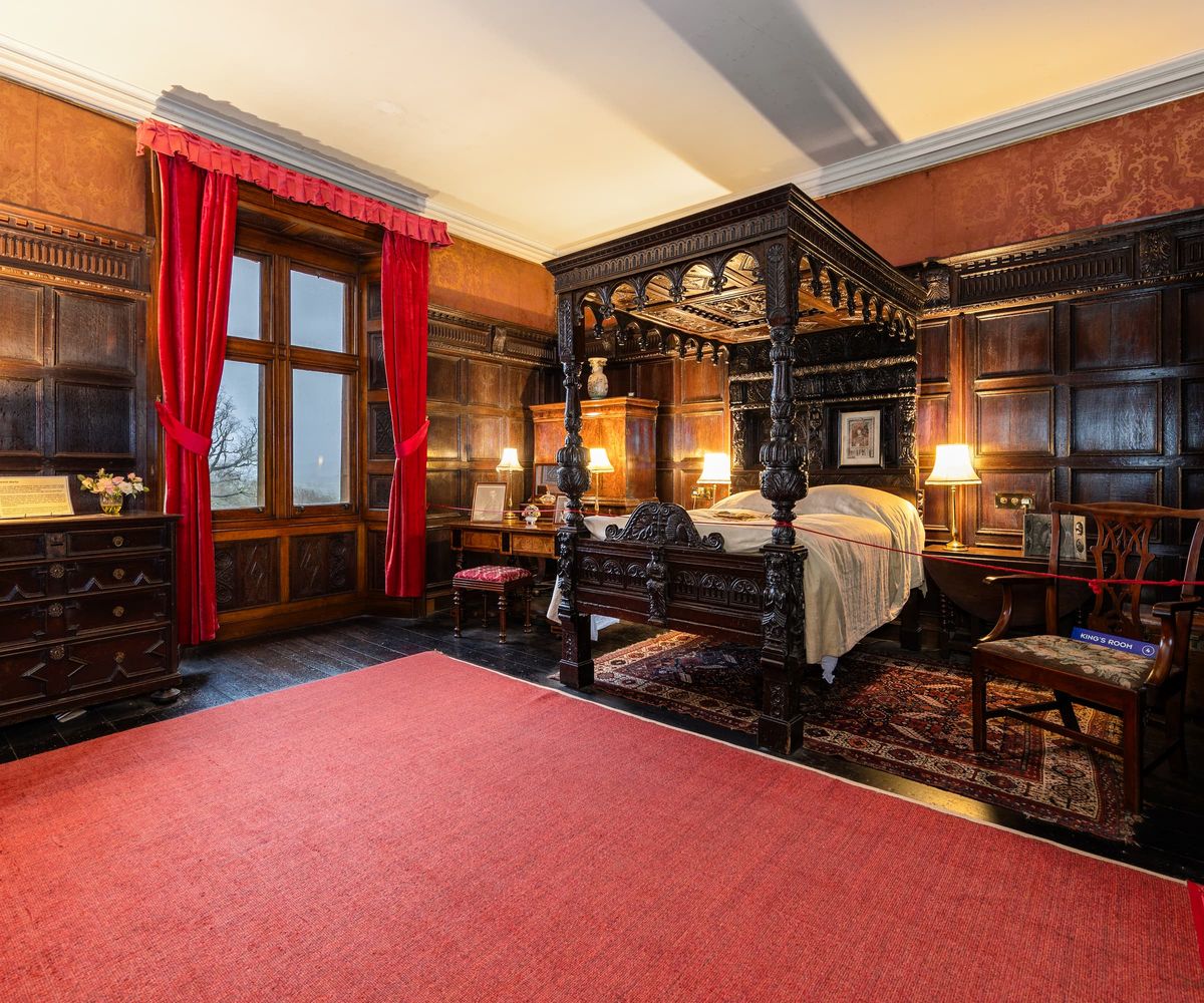 An old style bedroom with a four post bed and red carpet and old wooden floorboards