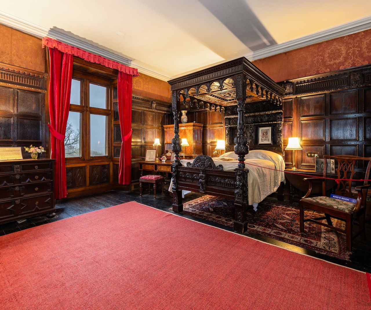 An old style bedroom with a four post bed and red carpet and old wooden floorboards