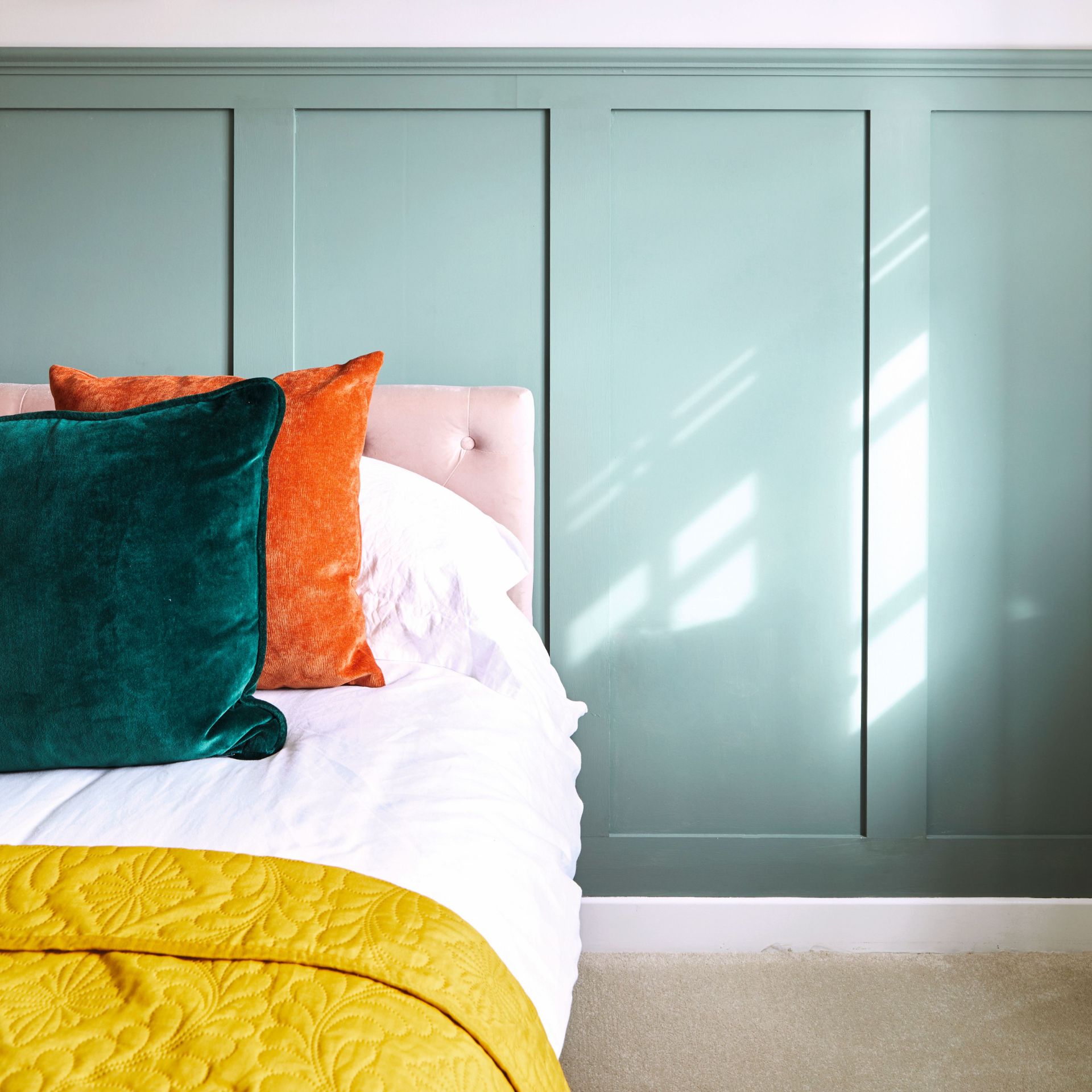 Bedroom with blue panelled wall, white bedding, orange and green cushions