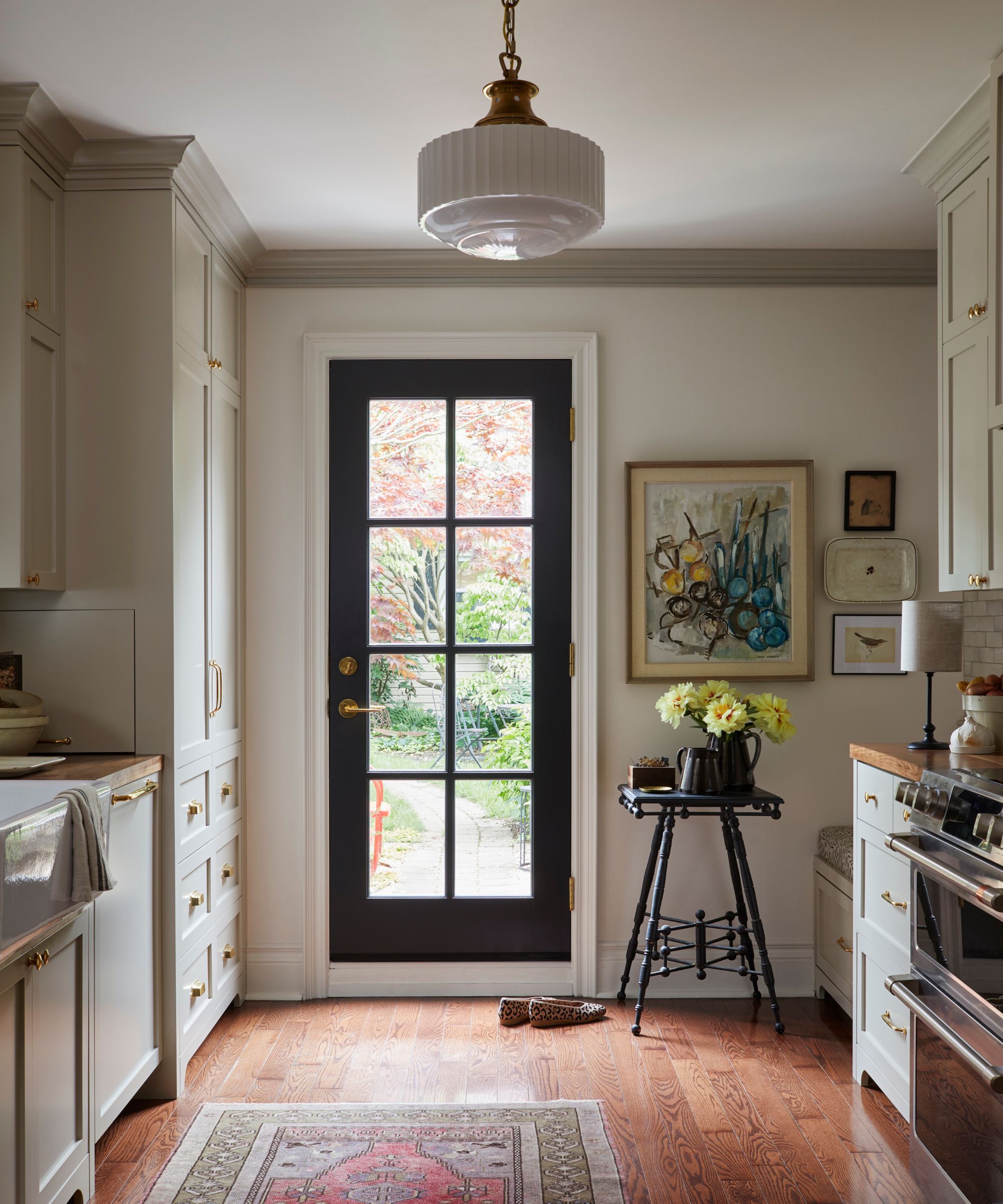 A galley kitchen with gray cabinets, a wooden floor topped with a red vintage rug, and white walls covered in collected art