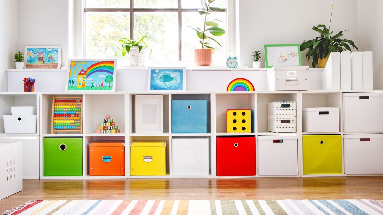 Bright white playroom with wall to wall two level cubby storage unit with colorful box drawers and bright crittal window in background