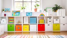 Bright white playroom with wall to wall two level cubby storage unit with colorful box drawers and bright crittal window in background