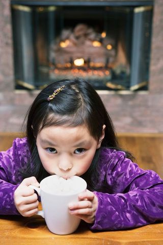 A young girl sips a mug of hot chocolate.