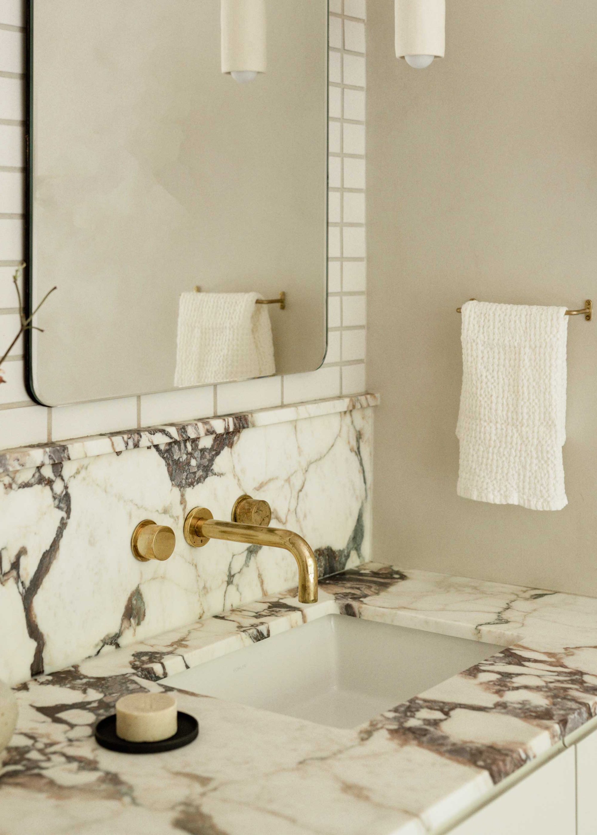 a marble bathroom countertop with gold hardware and a soap on a dish as well as a face towel hanging