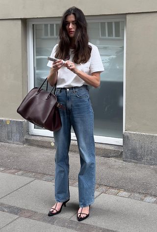 a photo of a woman wearing minimalist strappy heeled black sandals with jeans and a white T-shirt and a large tote bag