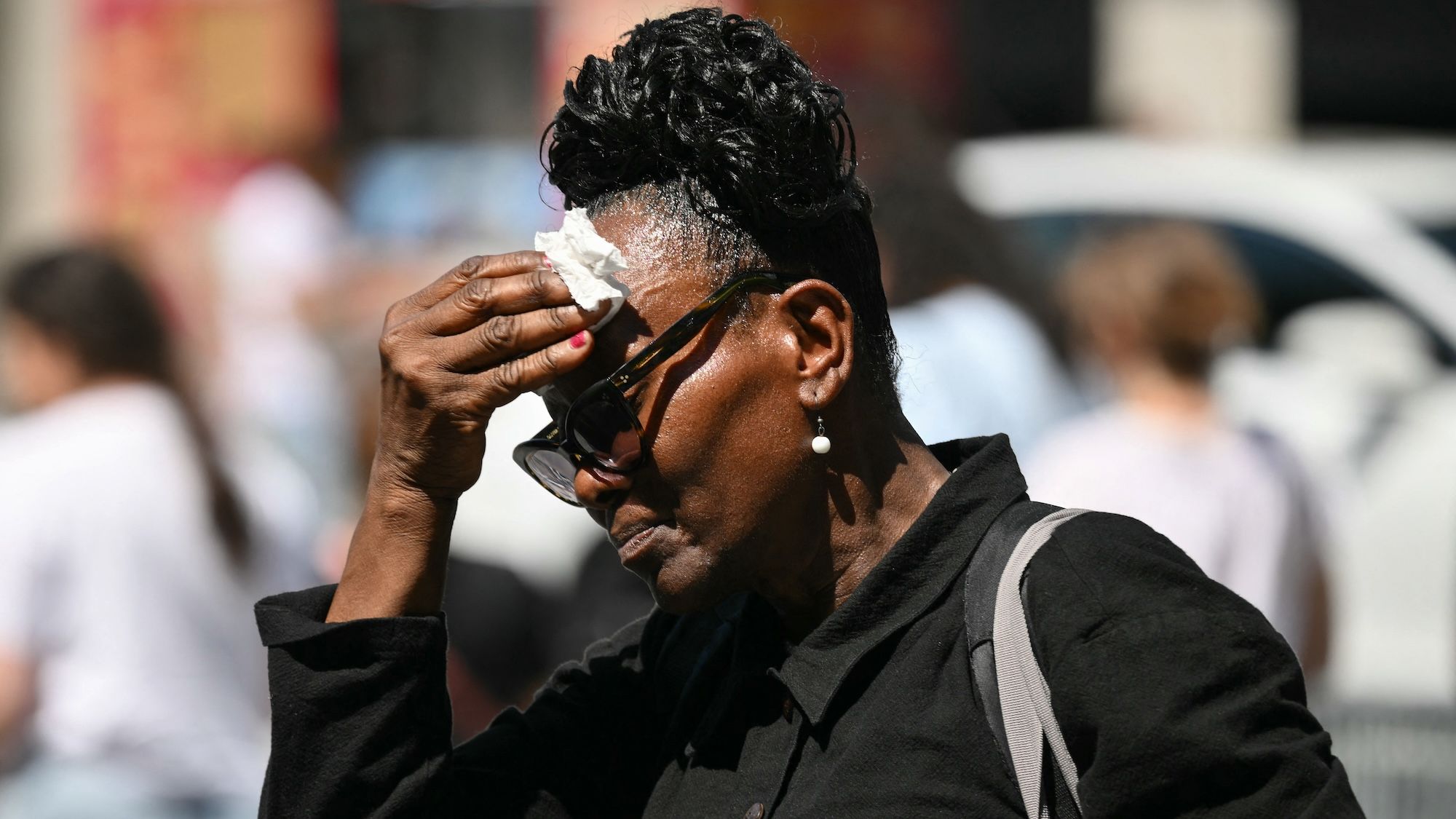 An older woman mops her head with a tissue in hot weather