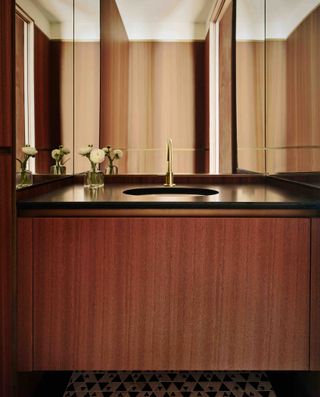 Black and wooden powder room with white basin and small vase with white rose