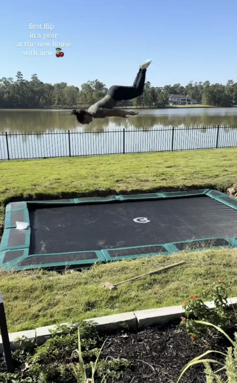 a photo of a woman doing a flip on a trampoline in a backyard in front of a lake