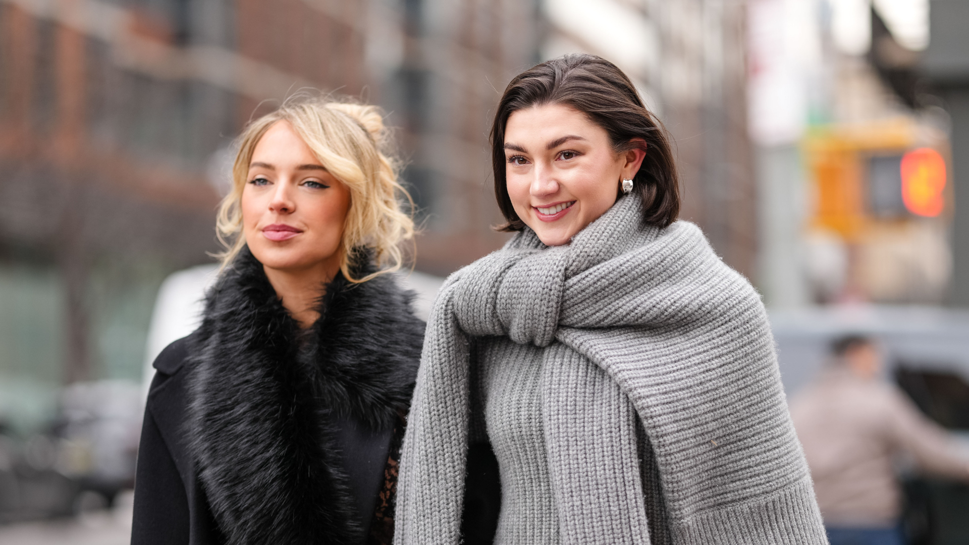 A guest wears black oversized Michael Kors coat, black faux fur scarf, black sheer mesh floral lace midi Michael Kors skirt, shiny black Michael Kors leather bag. Kate Bartlett wears black sunglasses, silver earrings, dark gray oversized knit Michael Kors sweater, light gray long sleeve Michael Kors sweater, dark gray midi Michael Kors skirt, white leather Michael Kors bag with silver chains, outside Michael Kors, during the New York Fashion week Fall/Winter 2025 on February 11, 2025 in New York, New York