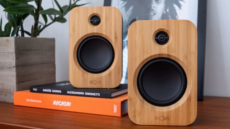 House of Marley Get Together Duo review: bookshelf speakers sitting on wooden unit with stack of books and framed Bob Marley print
