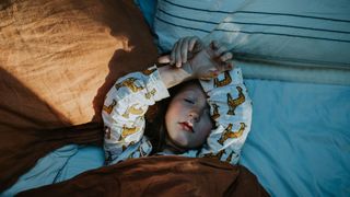 A kid sleeps in bed in a dark room