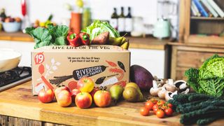 A riverford fruit and veg subscription box on a wooden kitchen surface