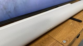 Sonos Arc Ultra soundbar in white on wooden bench underneath TV