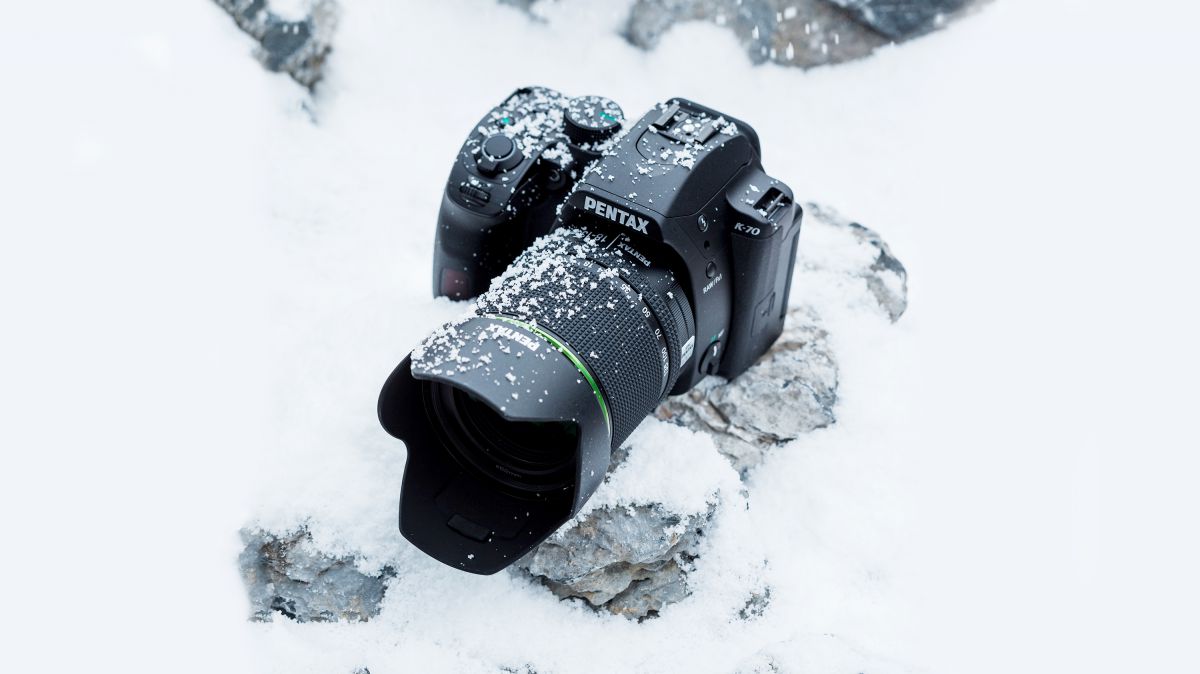 En Pentax K-70 ligger placerad på en sten med massor av snö runtom.