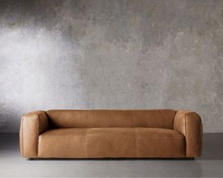 A tan leather couch in front of a concrete-textured wall