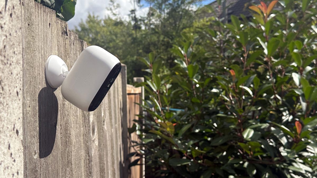 Arlo Essential 2nd Gen on fence with view over garden - shrubs and sky visible