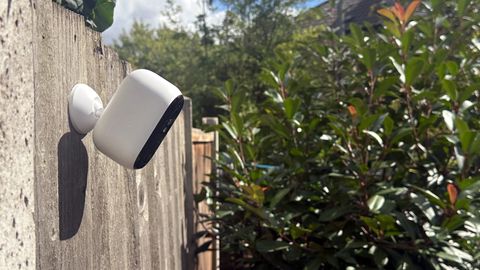 Arlo Essential 2nd Gen on fence with view over garden - shrubs and sky visible