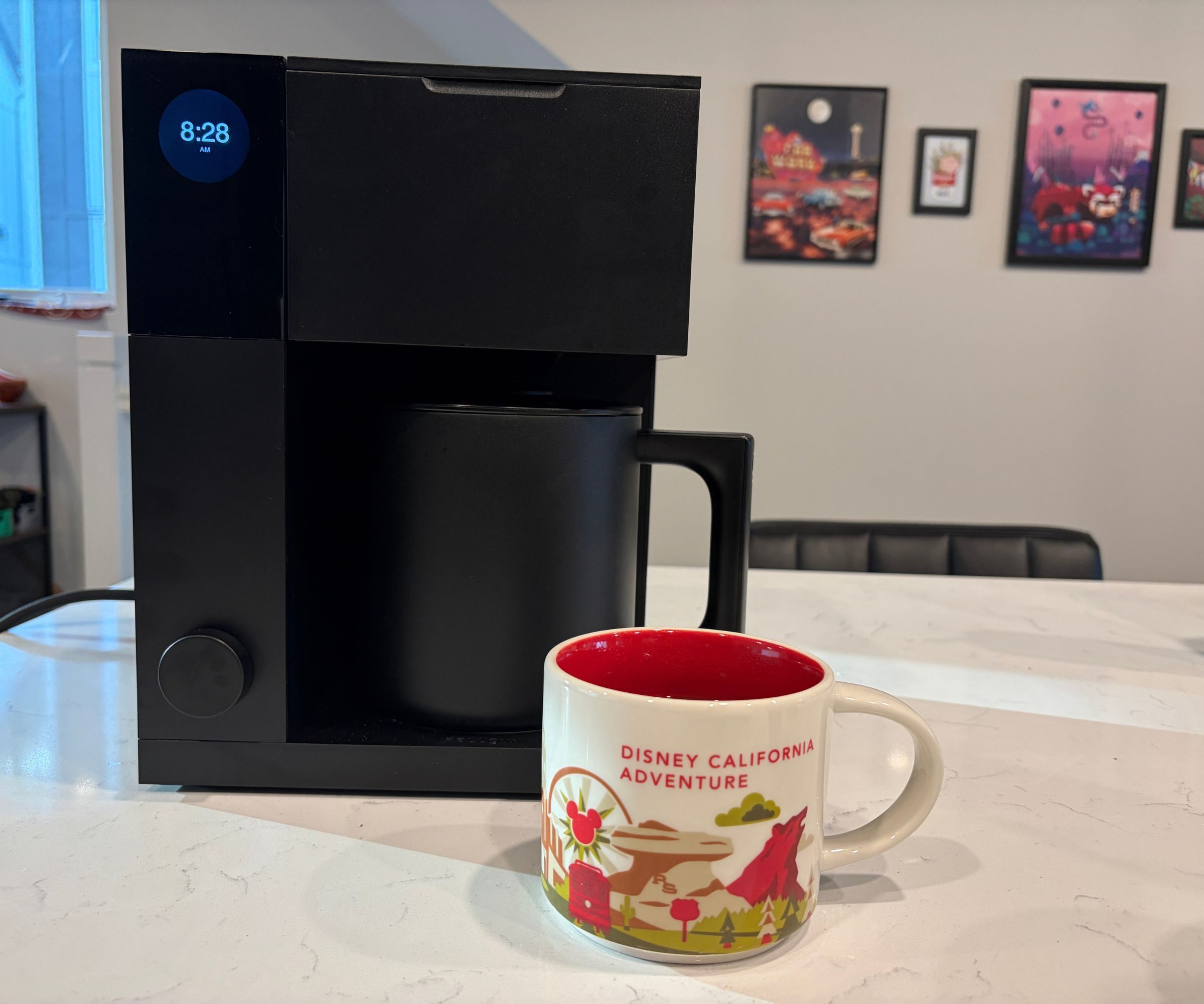 A large black coffee maker with a Disney mug in front of it on a white kitchen counter.