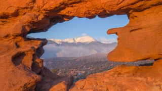A snow capped Pikes Peak seen through the Siamese Twins rock formation