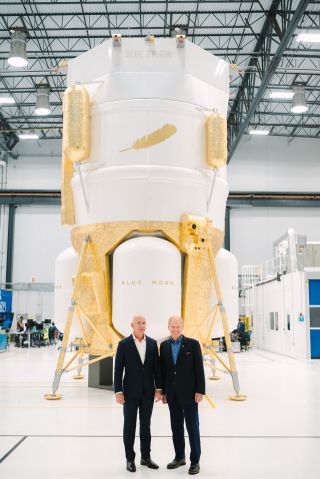 two men in suits in front of a gold-and-white capsule-shaped spacecraft
