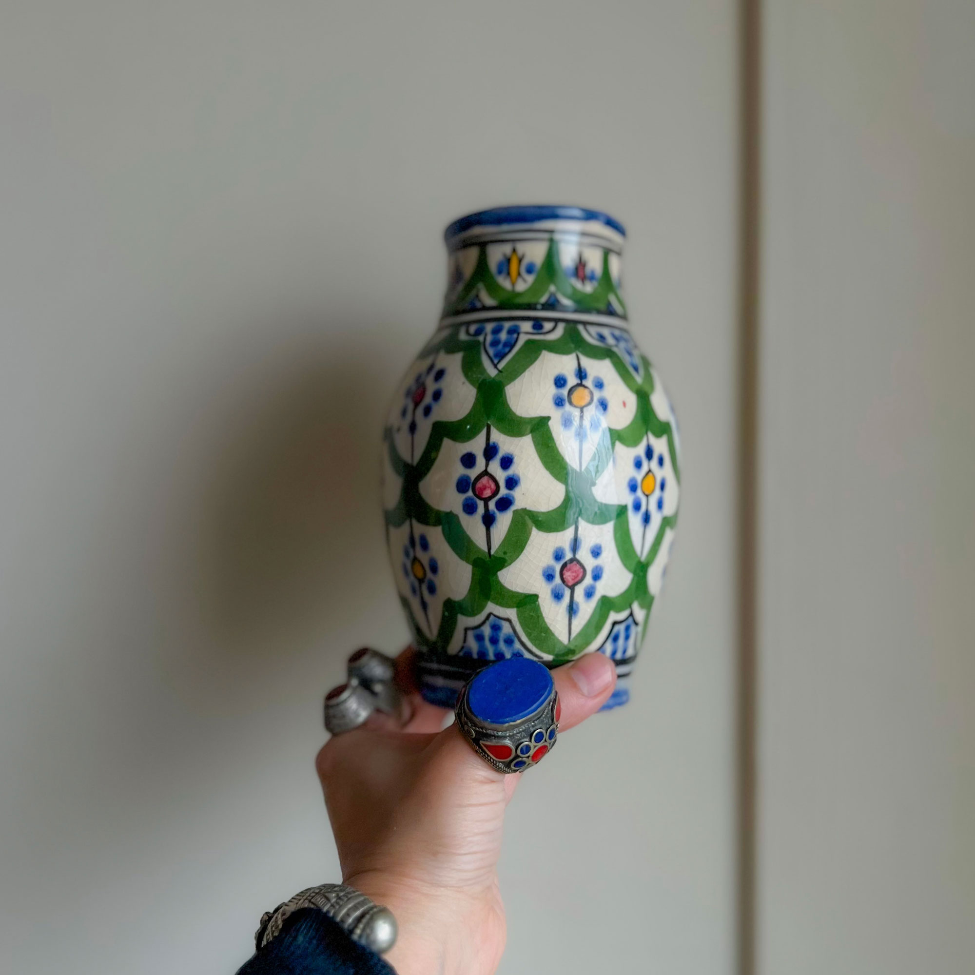 Woman wearing chunky rings holding up small green, blue and orange vase