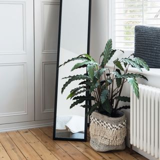 Standing mirror on a wooden floor beside pale grey built in wardrobe and window with venetian blinds