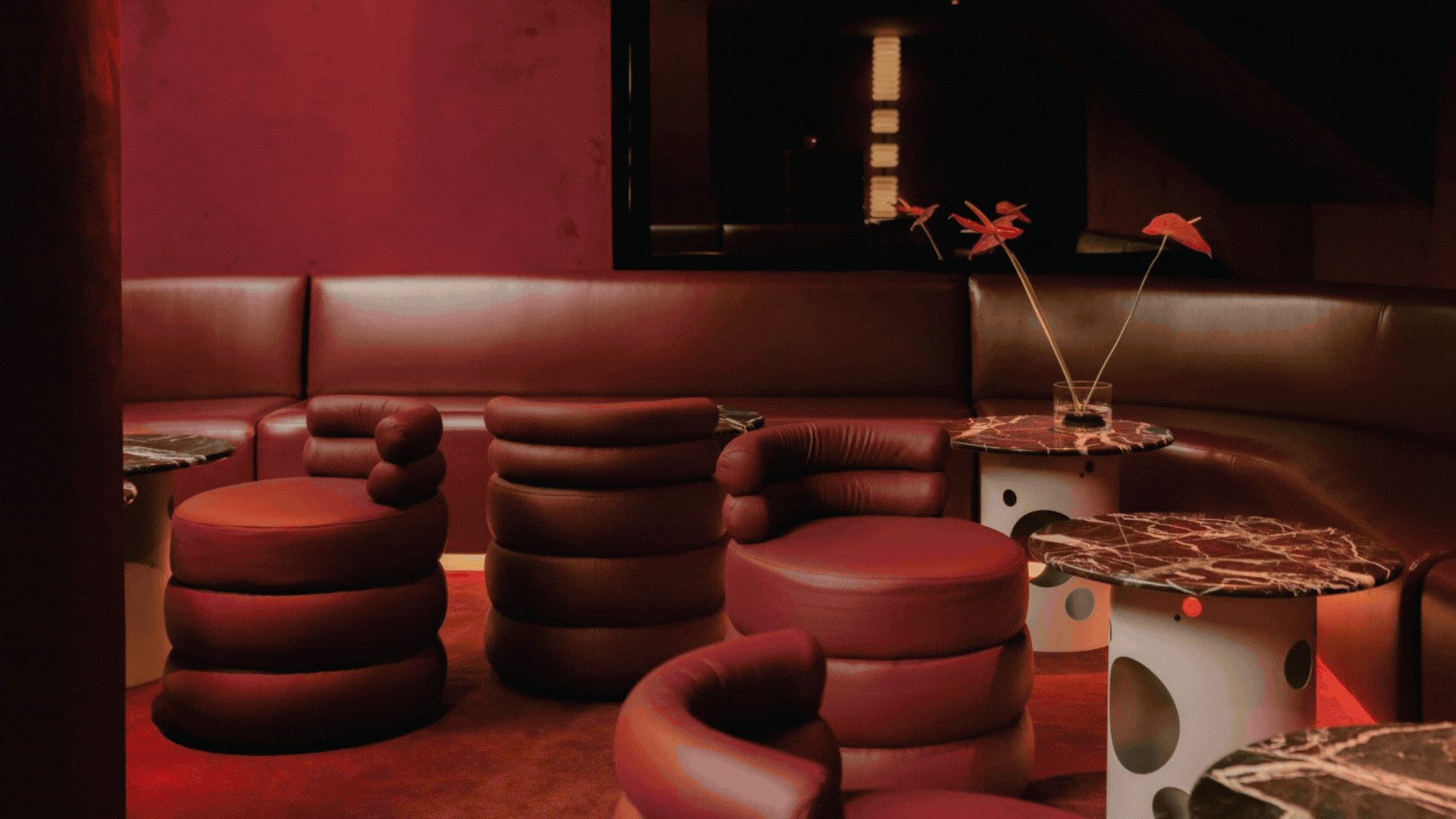 A rotating gif showcasing the red and orange-tinted interiors of a sophisticated cocktail bar with suffused lighting and textural finishes.