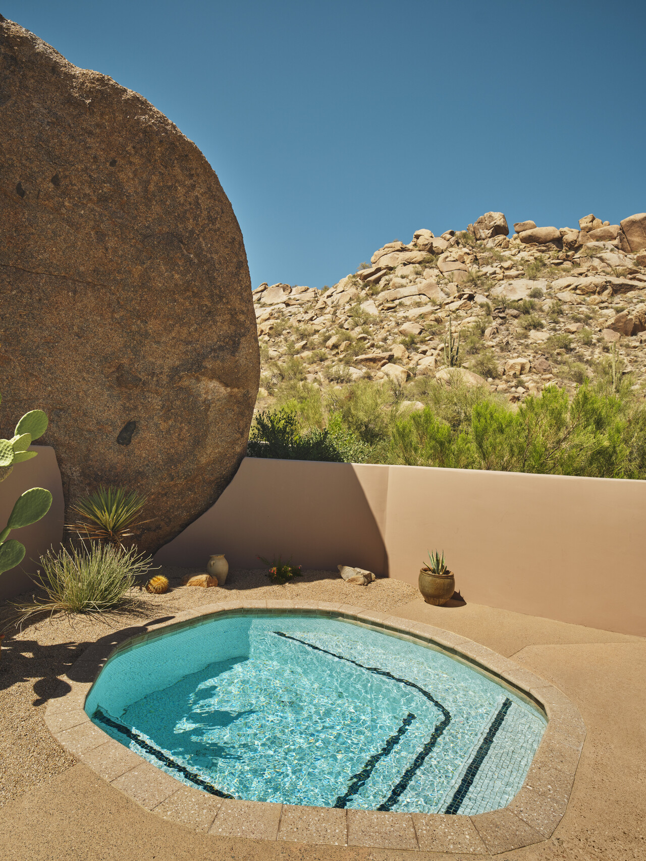 A sun-lit small pool built inside a terracotta patio immersed in desert nature.