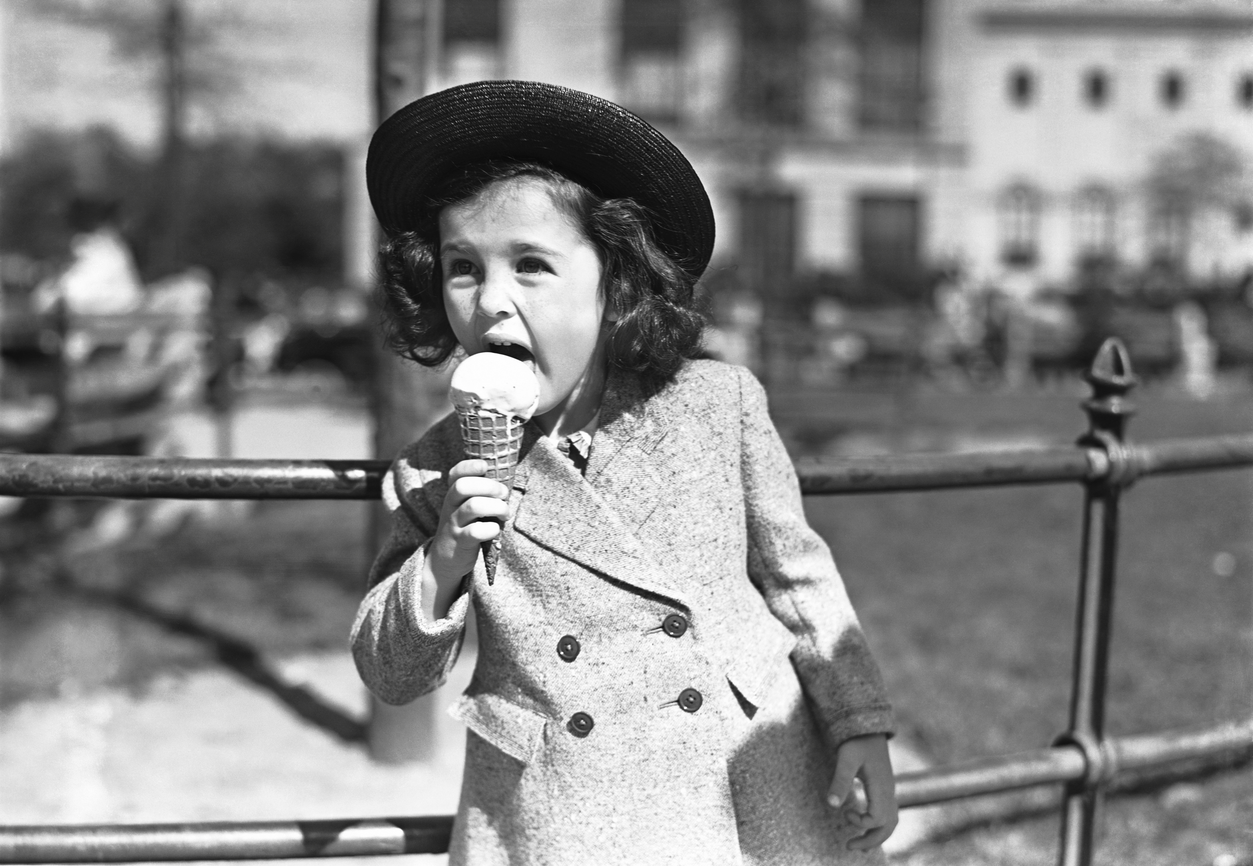 Black and white photograph of a young girl in a double breasted coat and hat eating an ice cream cone