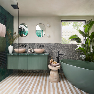 Green bath and cabinet with green tiles on the wall. The sinks are pink and there is a pink striped floor