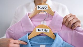 Woman holding two coat hangers with clothes and signs: declutter and keep