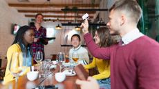 Young man giving a credit card to a waitress at the restaurant and paying for lunch for a group of friends.