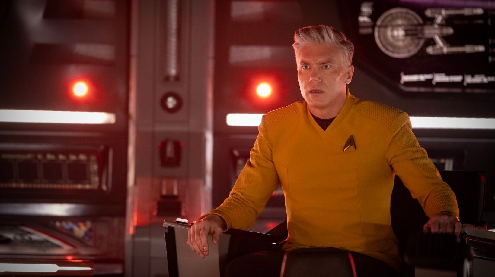 A man wearing a yellow uniform sat in the captain's chair aboard a starship. He looks shocked.