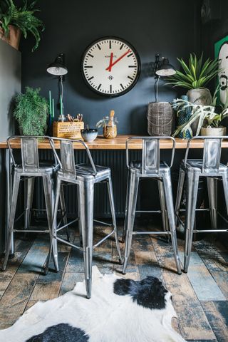 kitchen breakfast bar with industrial bar stools, dark walls, a large clock and a cow hide rug