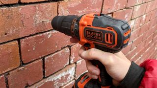 Person holding orange and black Black & Decker drill drilling into red brick wall 