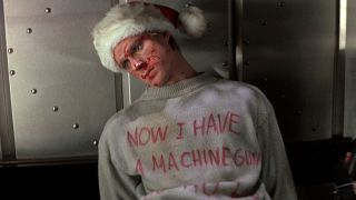 A still of a defeated bad guy wearing Santa hat and a jumper that reads "Now I have a machine gun, ho, ho, ho" in Die Hard