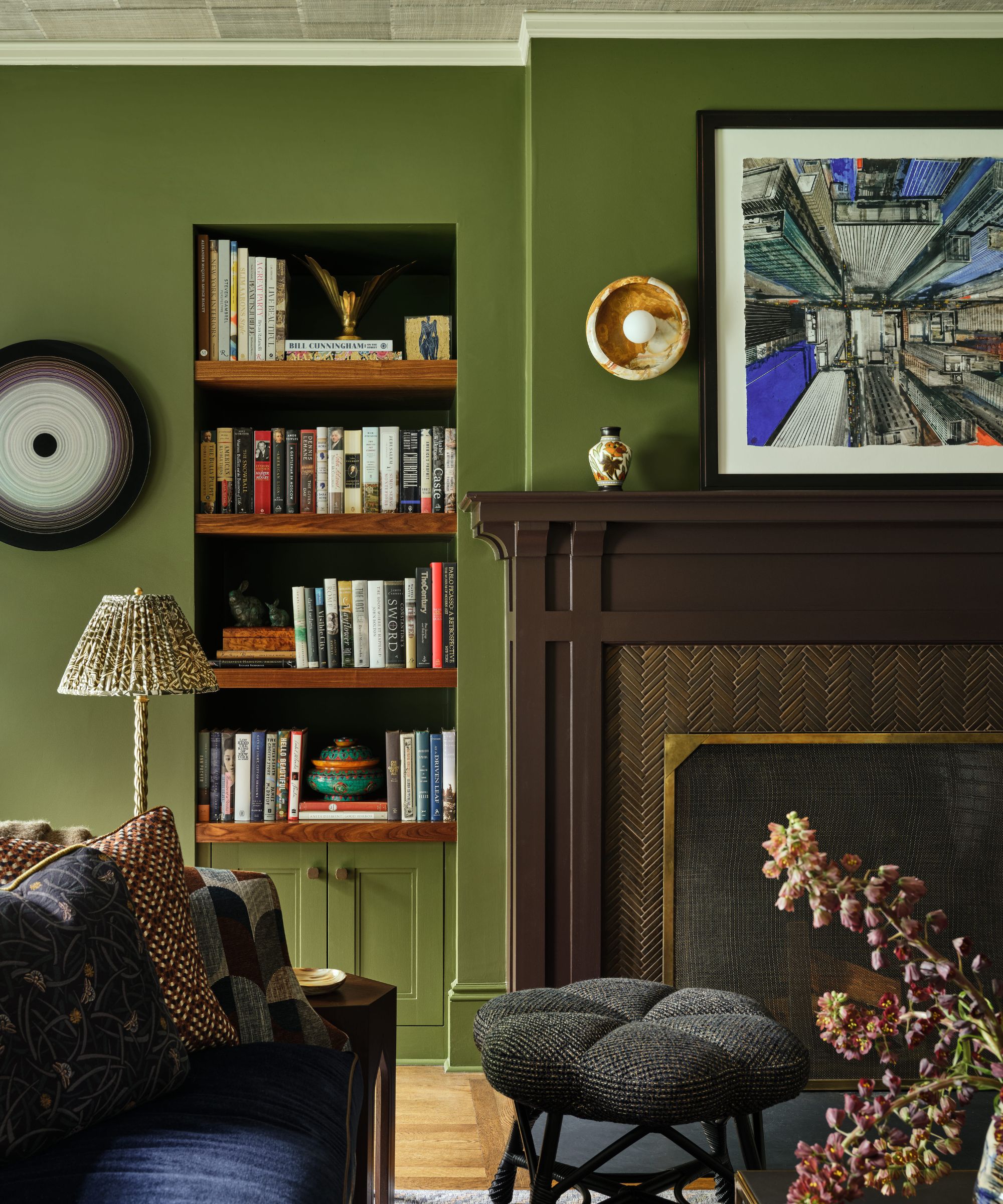 Green living room wall with a dark brown fireplace mantel, built-in bookshelf, and framed architectural art.