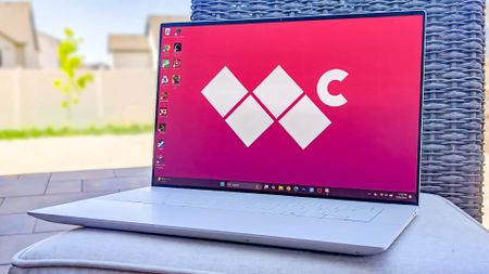 The Dell 16 Premium outside on a cushion with a patio backdrop. The Windows Central logo is on the laptop's background screen. 