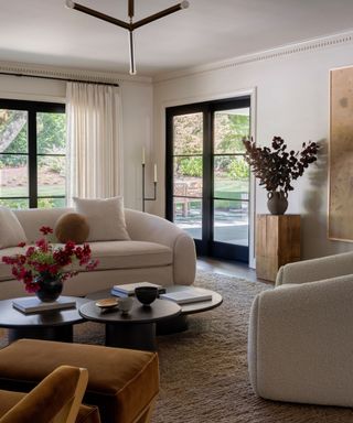 neutral modern living room with white walls, glass doors, beige sofa, black coffee circular coffee tables