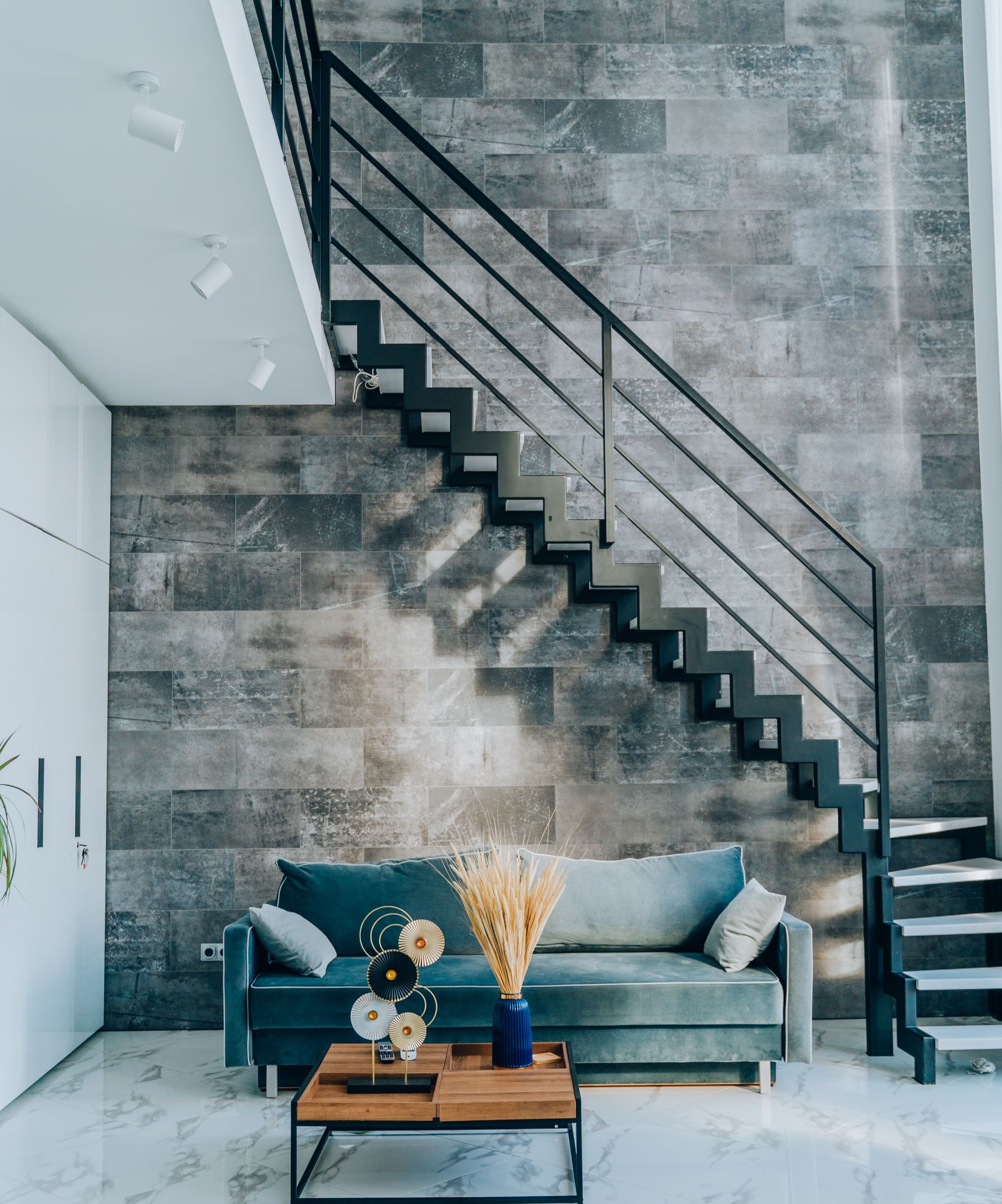 A black metal staircase with metal handrail and a velvet sofa beneath with a wooden coffee table