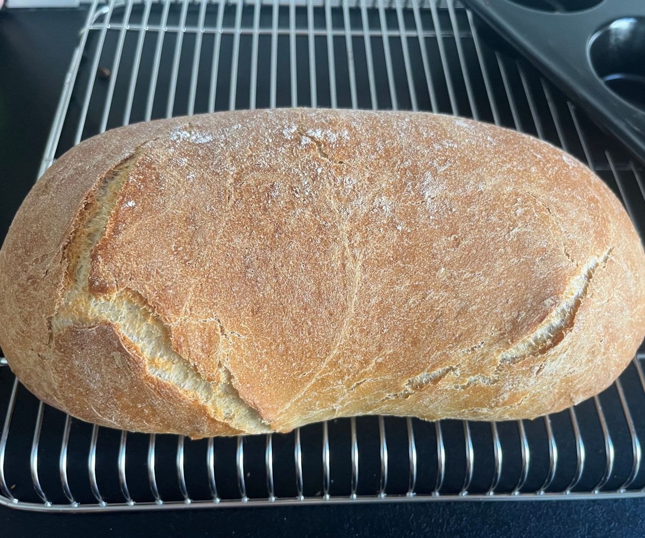 A crusty oval shaped bread loaf on a cooling rack