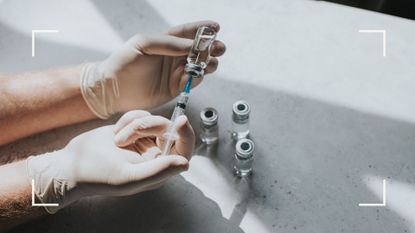 Person preparing dose of Covid-19 vaccine with white gloves on over marble worksurface