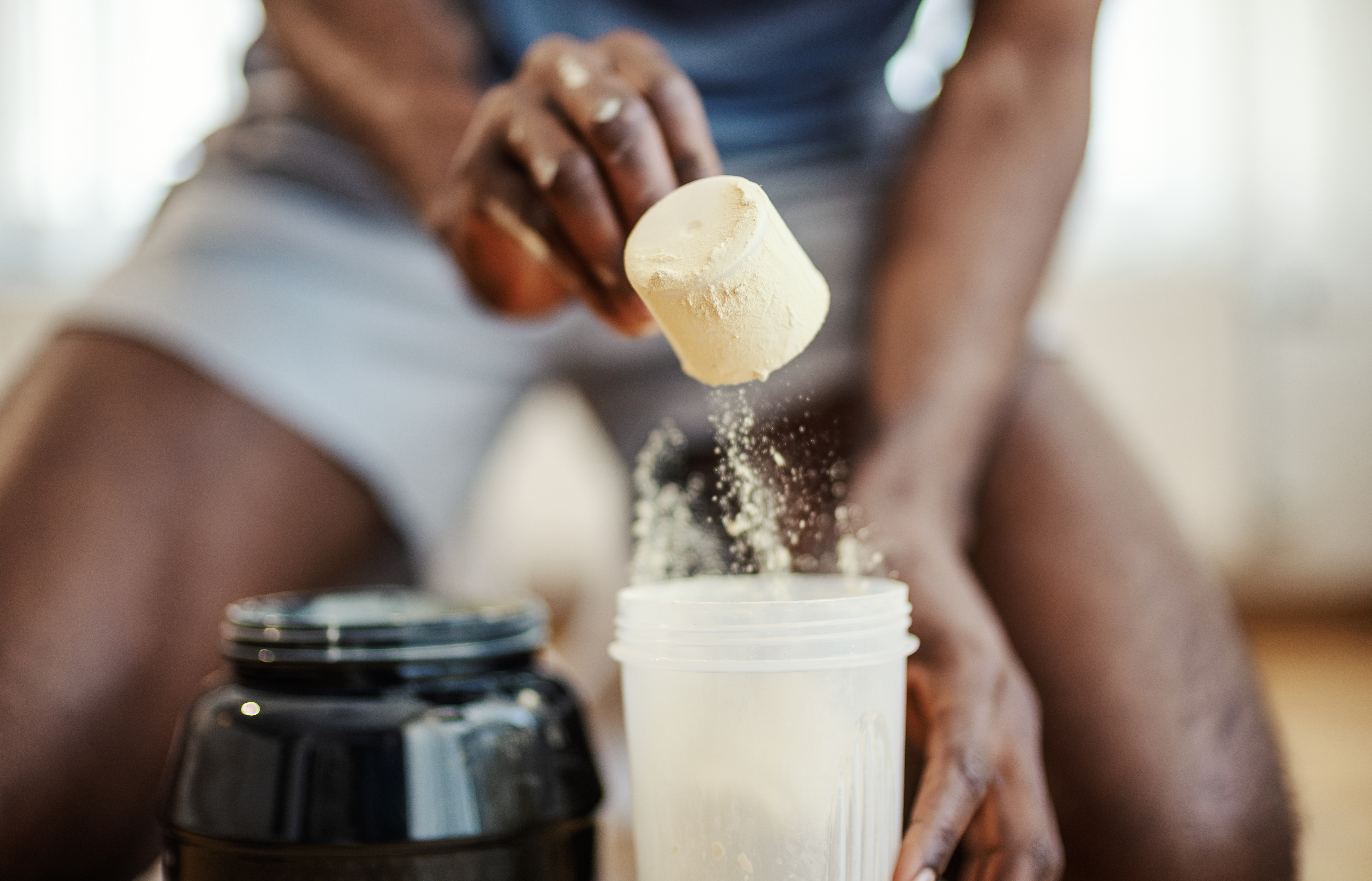 Man pouring protein powder into a shaker bottle with a scoop