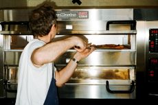 A pizzamaker pulling a pizza out of a chrome-clad oven.