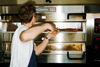 A pizzamaker pulling a pizza out of a chrome-clad oven.